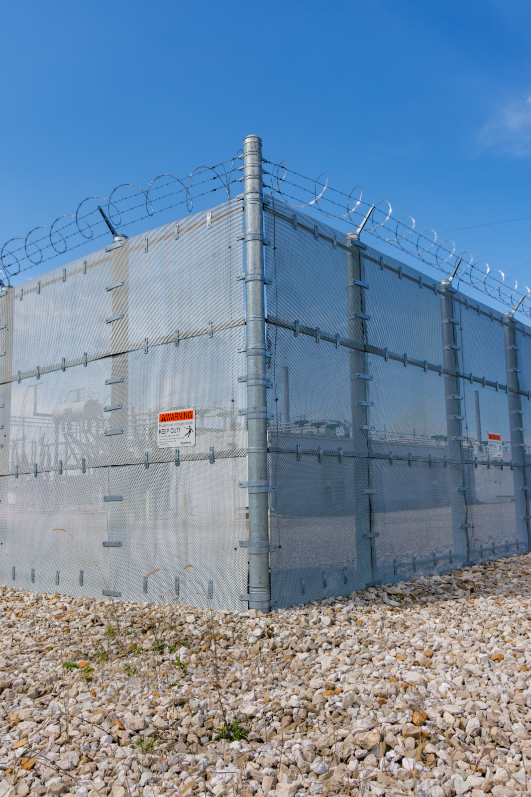 Solid-panel security fence with razor wire and "Hazardous Voltage — Keep Out" warning signage at the substation perimeter.